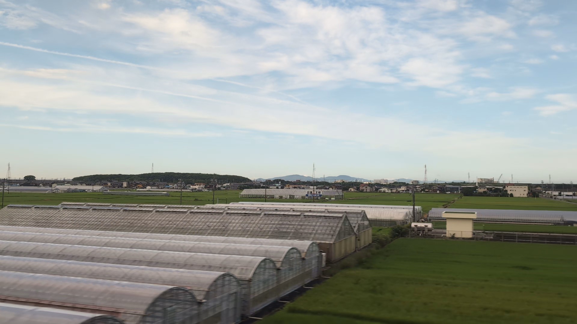 Curved greenhouse roofs close to the train, with pointed roofs and green fields beyond