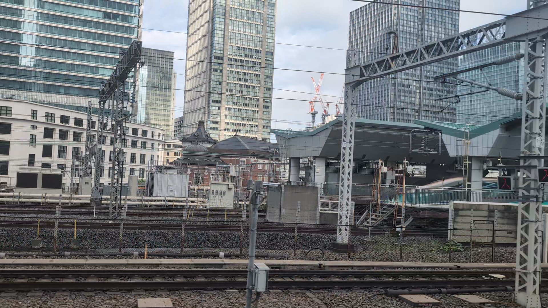 Red brick and a Tokyo Station dome behind platforms and overhead wires, with high-rise buildings beyond