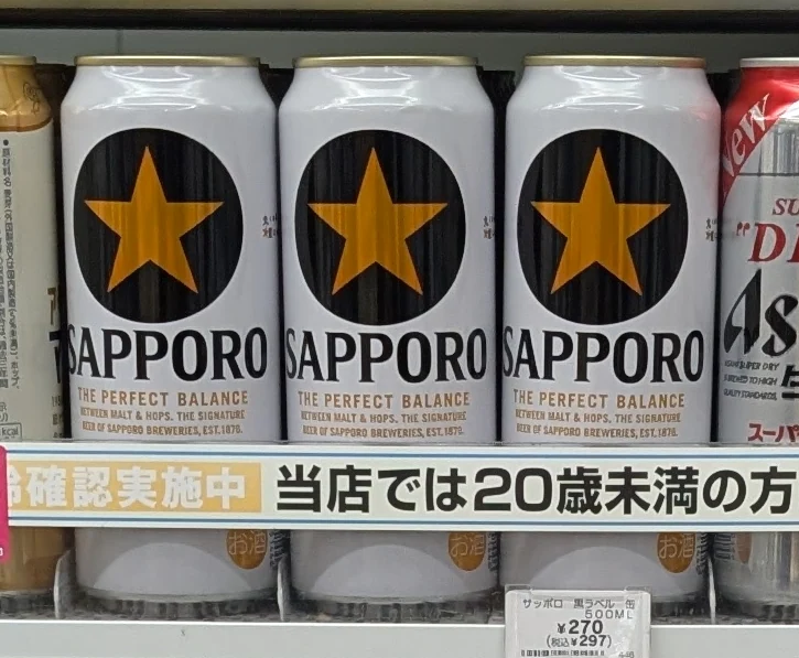 Three Sapporo Black Label cans with a gold star inside a black circle on a shop shelf.