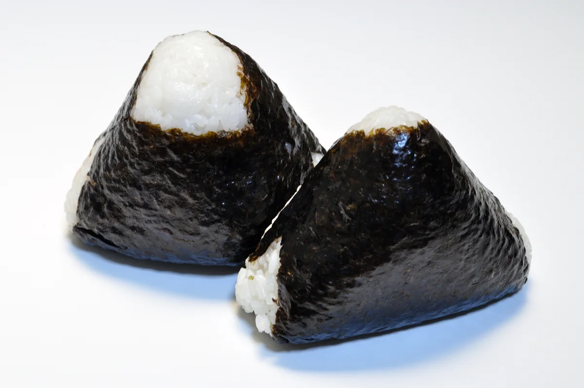 Two triangular onigiri rice balls wrapped in nori on a plate.
