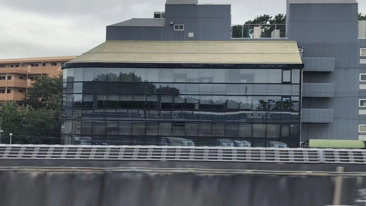About a minute after Shin-Yokohama, the Shinkansen reflected in the long windows of a trackside building
