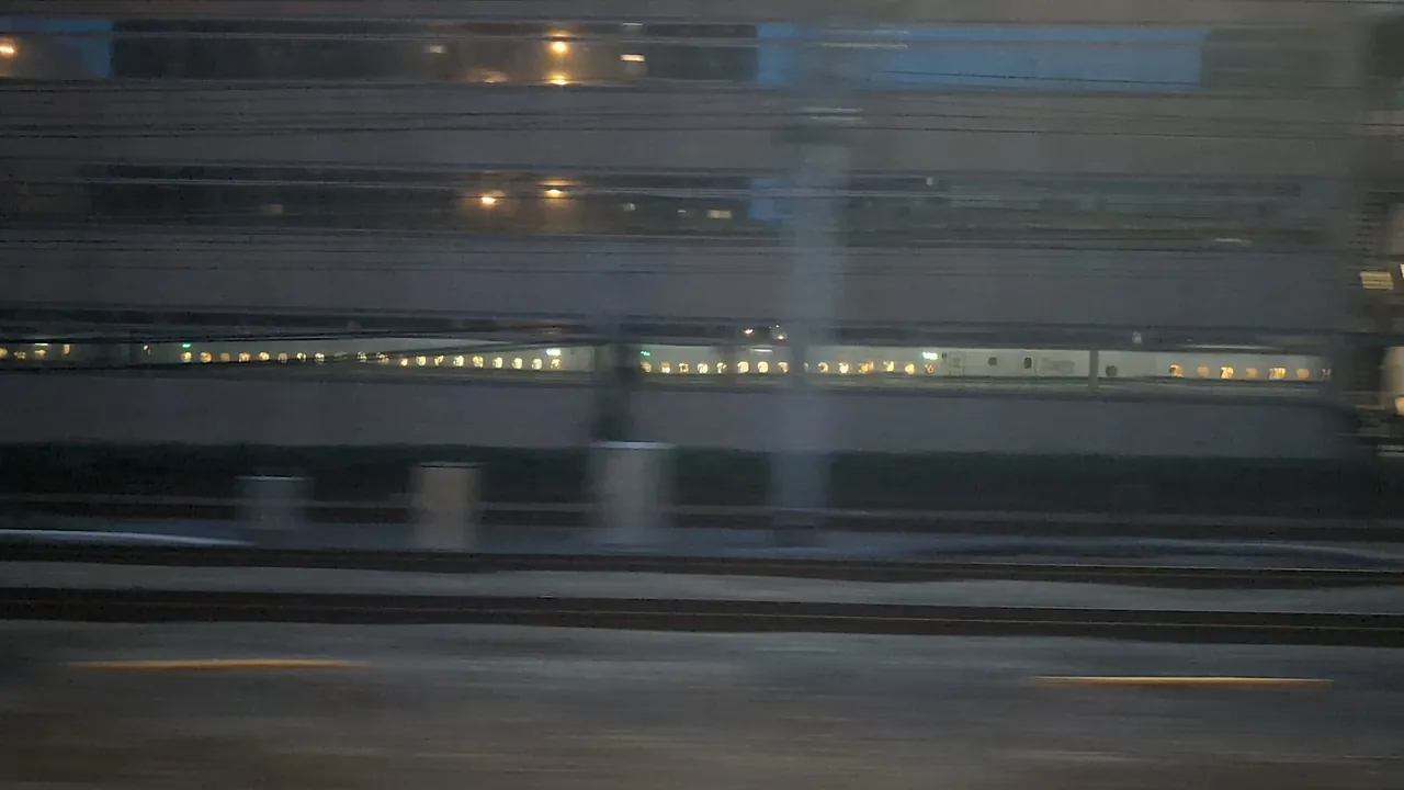 At night, a line of the train's window lights passing through the glass of a trackside building