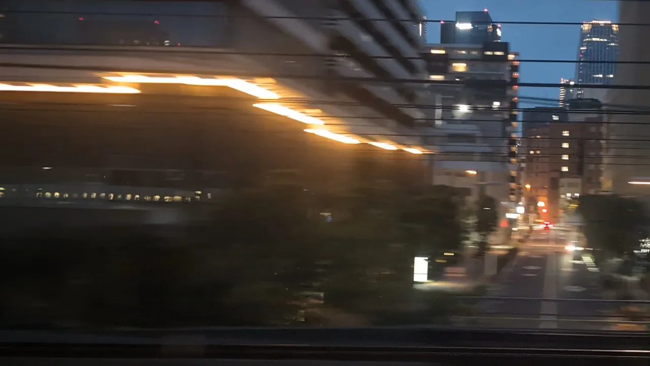 A night street; the train's window lights reflected low in the glass of the building on the left