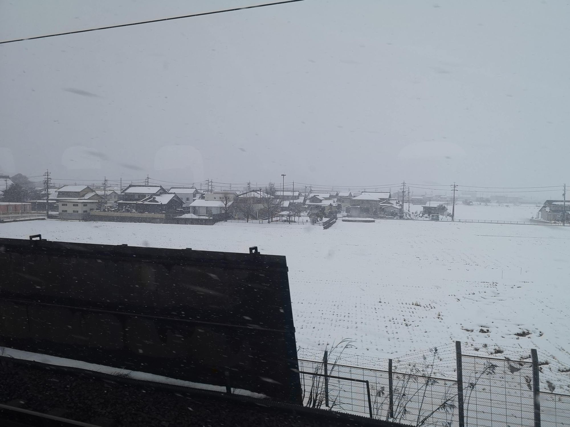 雪に覆われた田畑と集落を東海道新幹線の車窓から見る